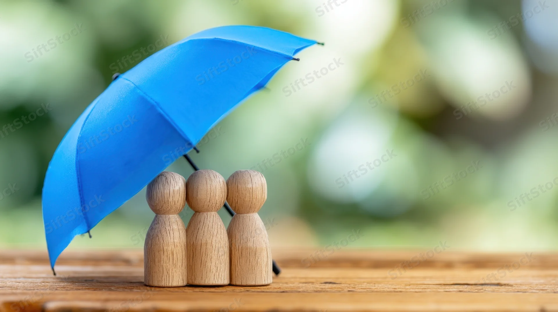 Three wooden figures under a blue umbrella on a wooden table