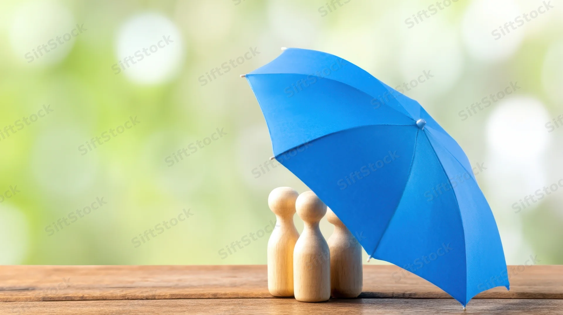 Three wooden figures under a blue umbrella on a wooden table