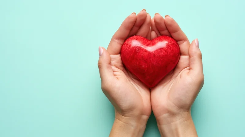 Hands holding a red heart against a light blue background