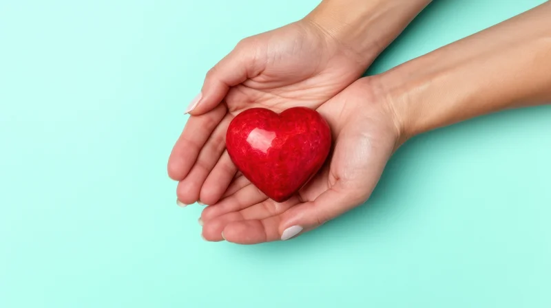 Woman's hands holding a red heart symbol against turquoise background