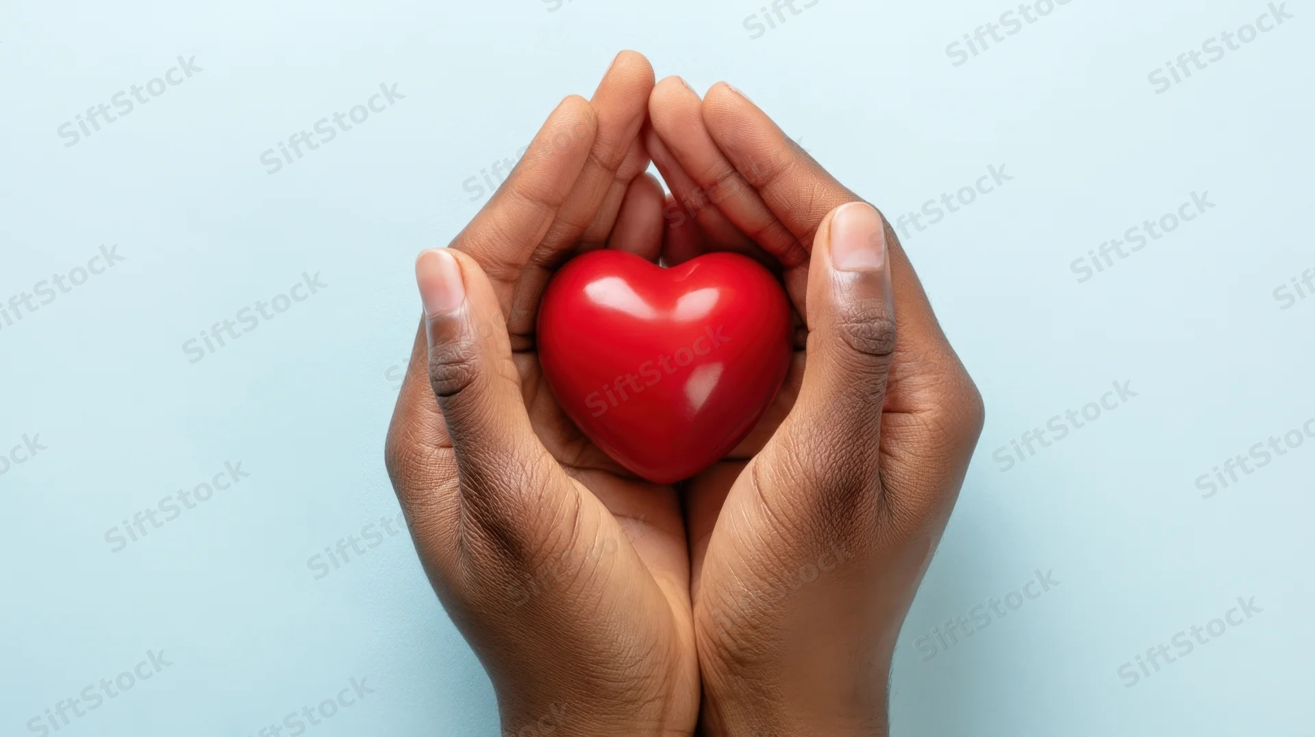 Hands holding a red heart against a light blue background