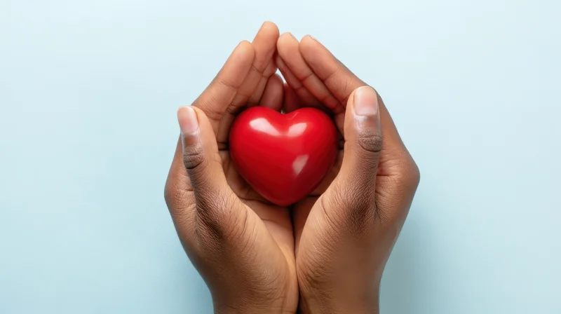 Hands holding a red heart against a light blue background