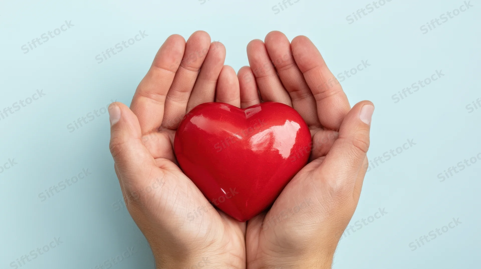 Hands holding a red heart against a light blue background