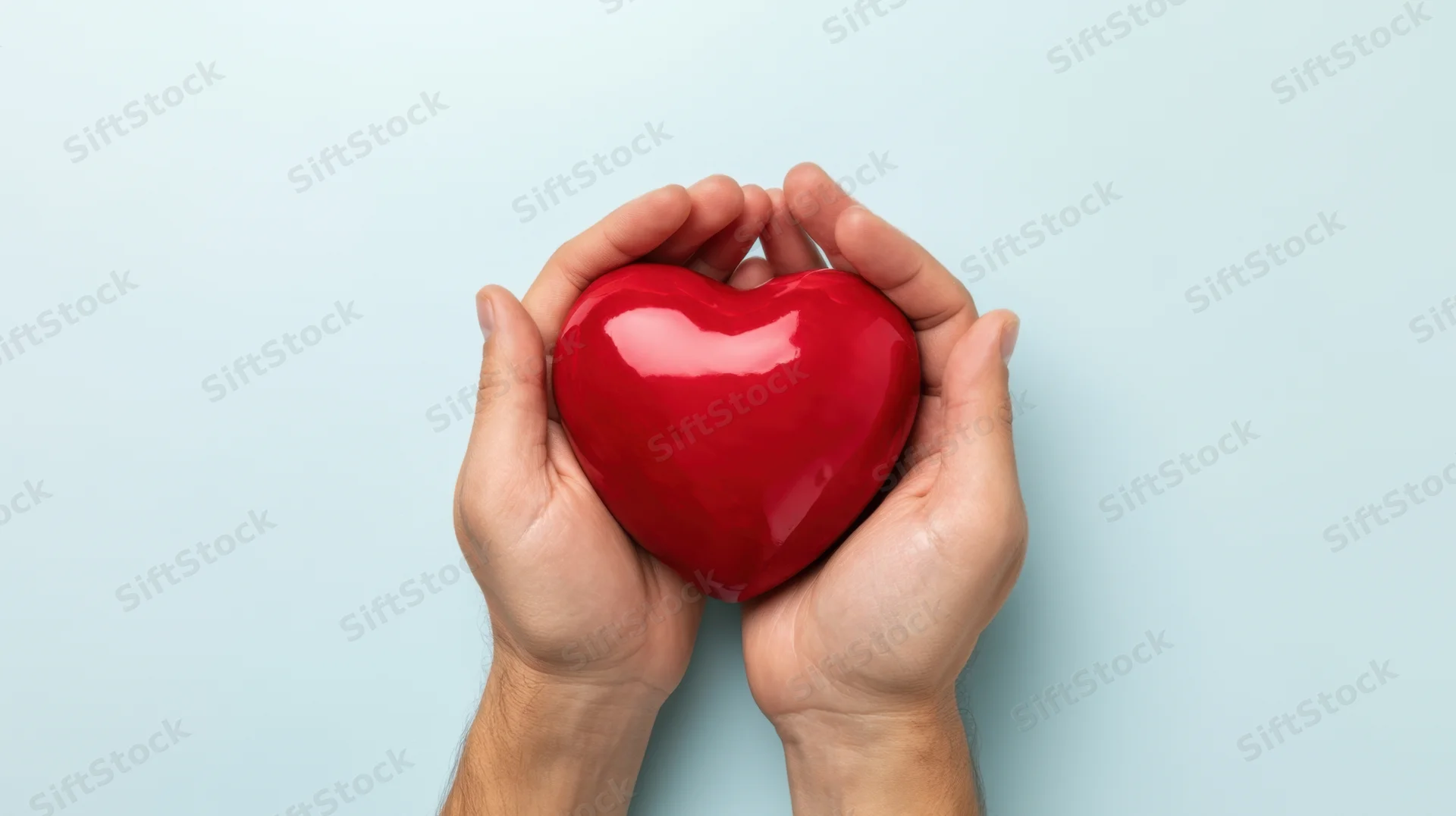 Hands holding a red heart against a light blue background