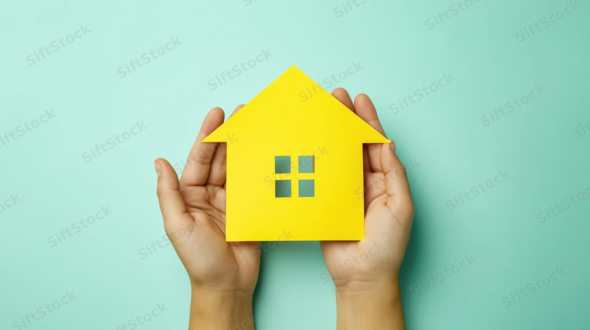 Hands holding a yellow paper house cutout against a mint background