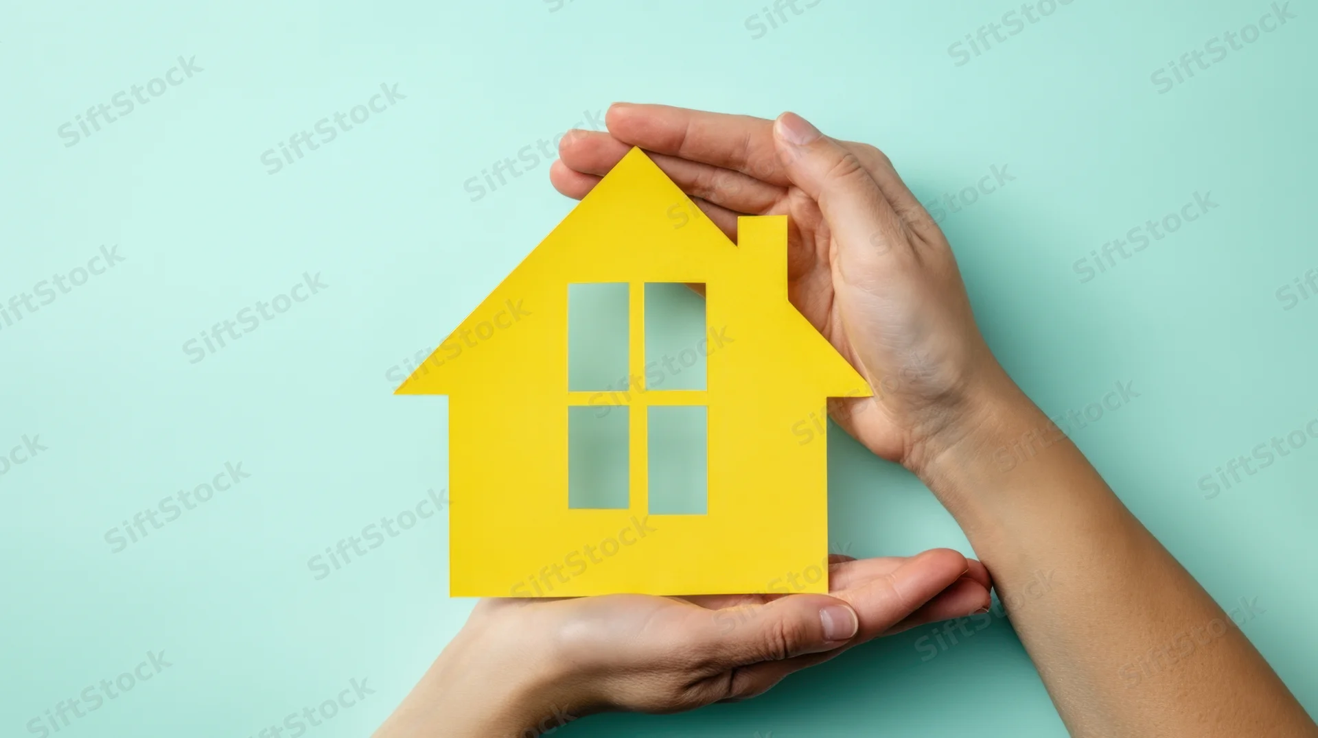 Hands holding a yellow paper house cutout against a teal background