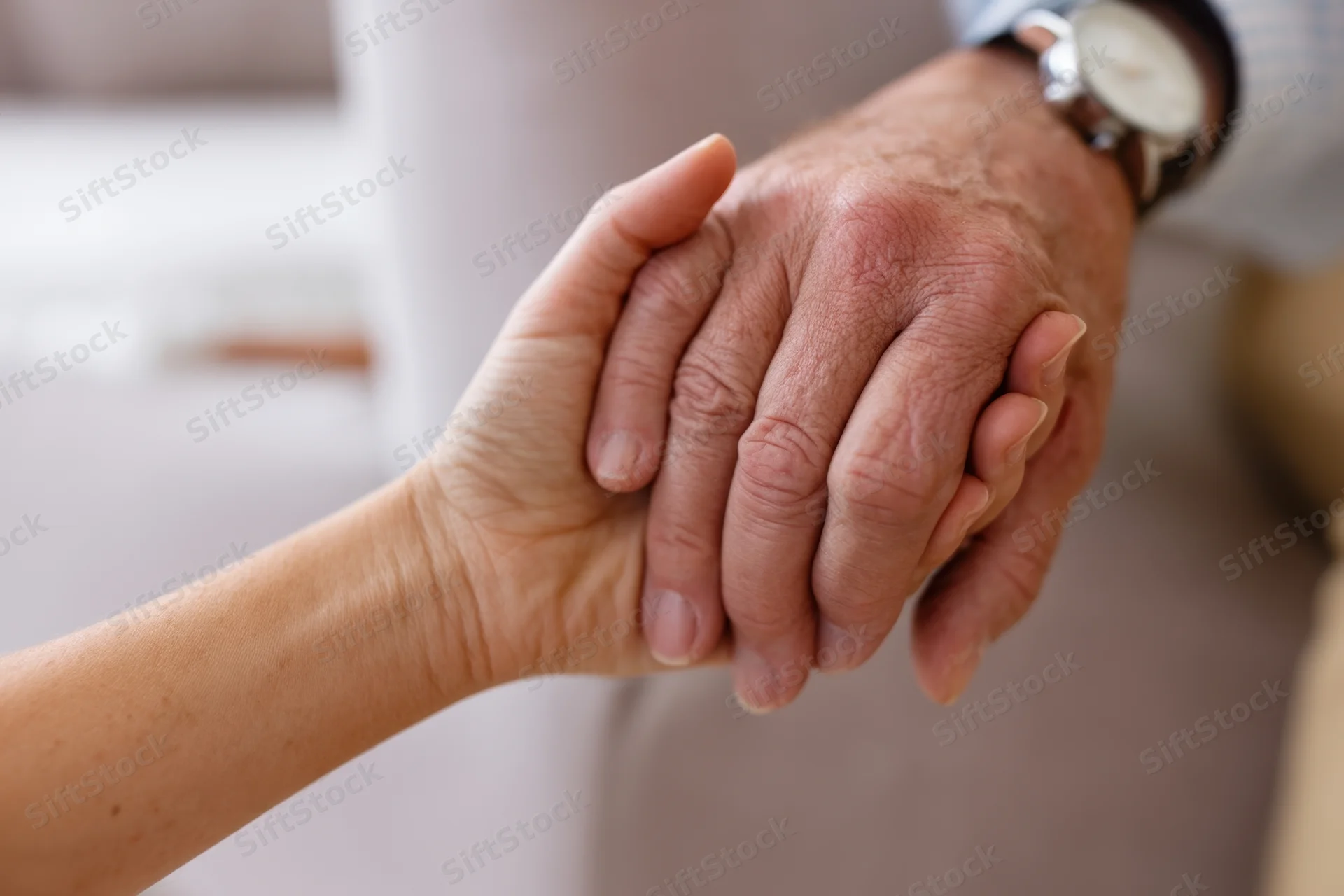 Woman's hand holding an elderly man's hand in a supportive gesture indoors