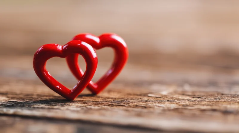 Two red heart ornaments interlocked on a wooden surface