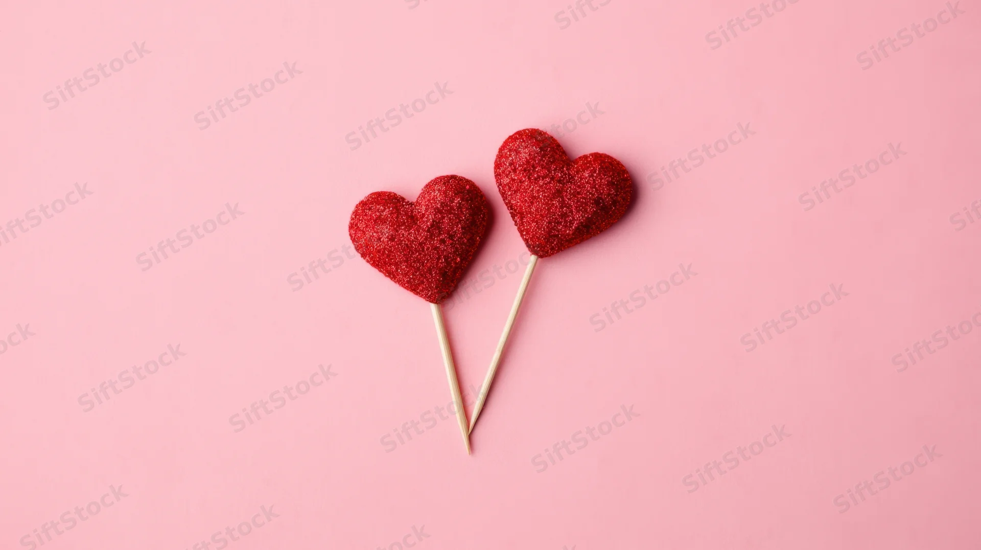Two red glitter hearts on sticks against pink background