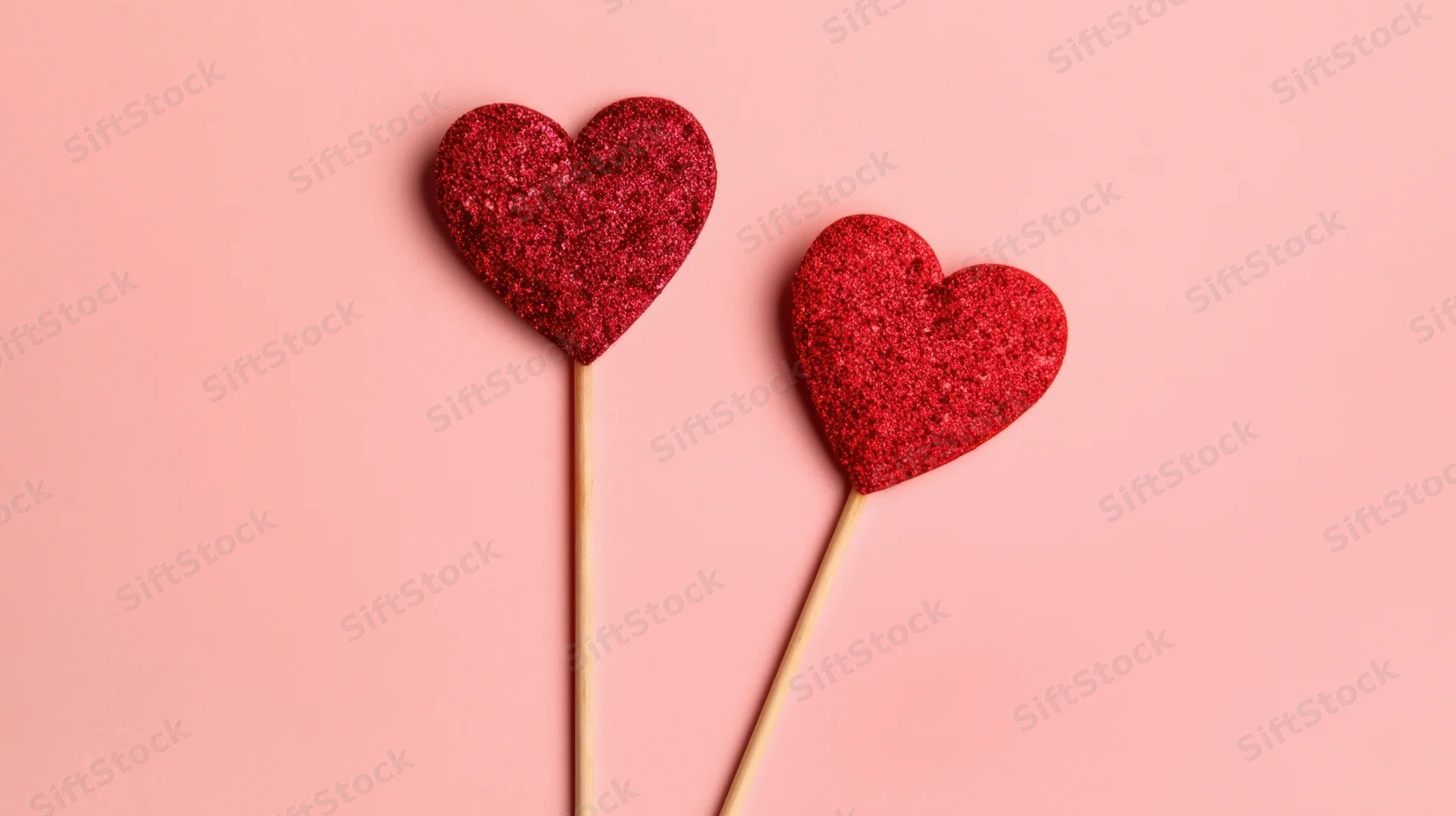 Two red glitter hearts on sticks against pink background