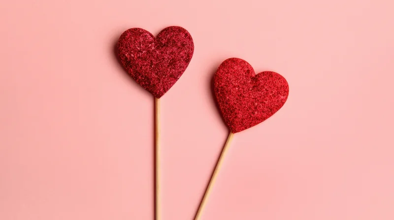 Two red glitter hearts on sticks against pink background