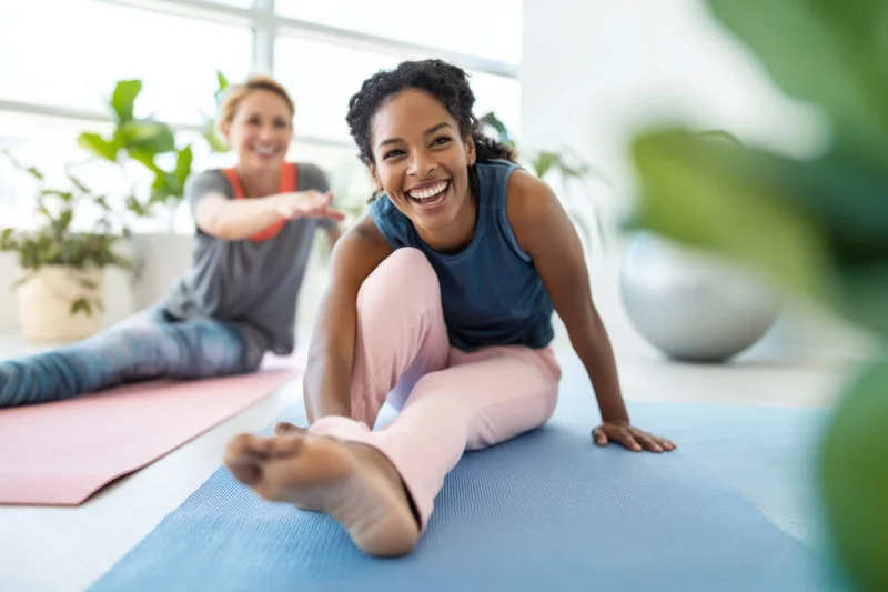 Two women stretching on yoga mats in a bright indoor studio