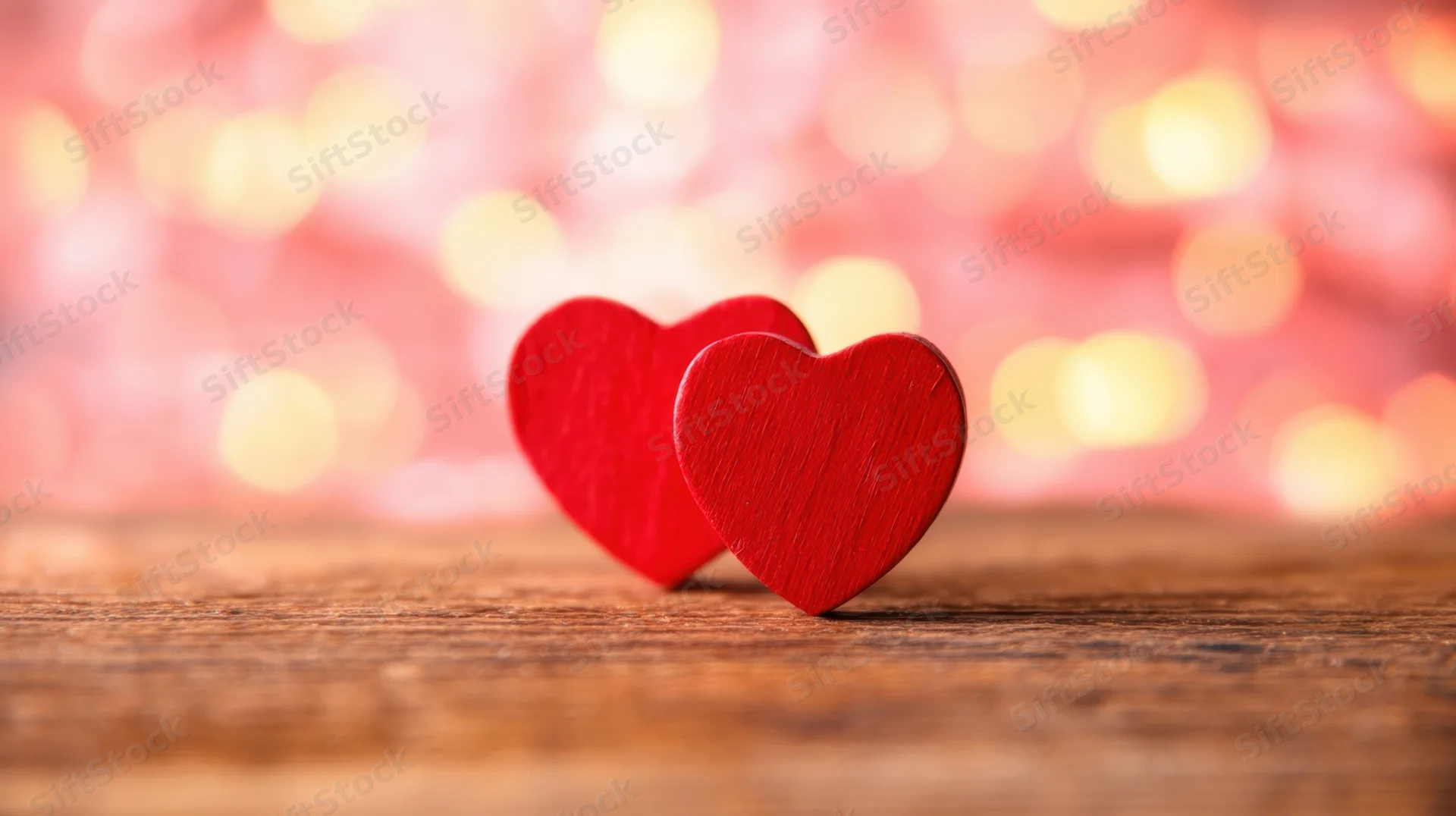 Two red wooden hearts on a wooden surface with blurred warm lights behind