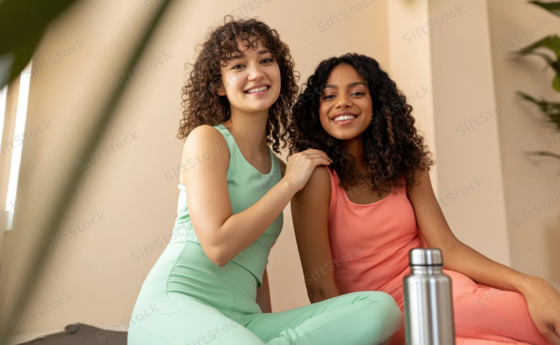 Two young women smiling while sitting together indoors in workout clothes