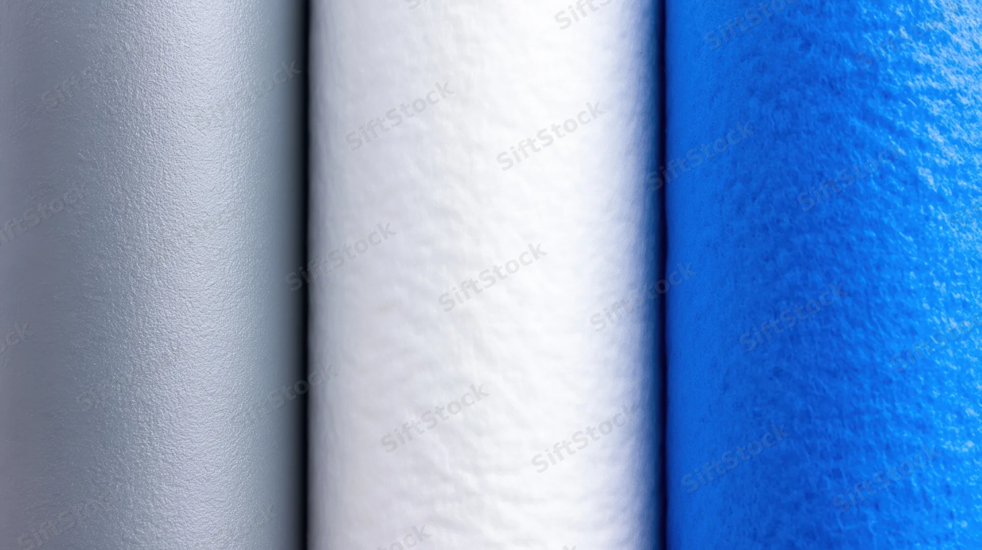 Closeup of three rolled water filtration membranes in gray, white, and blue arranged side by side