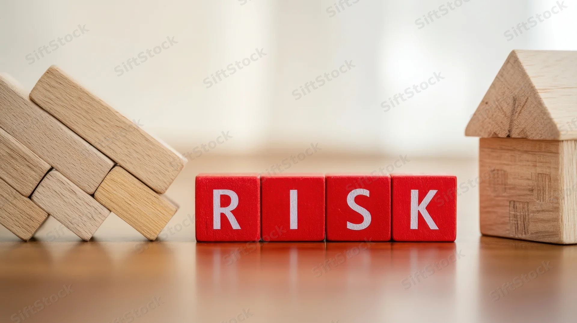 Red wooden blocks spelling risk between a collapsing stack and a small house on a table