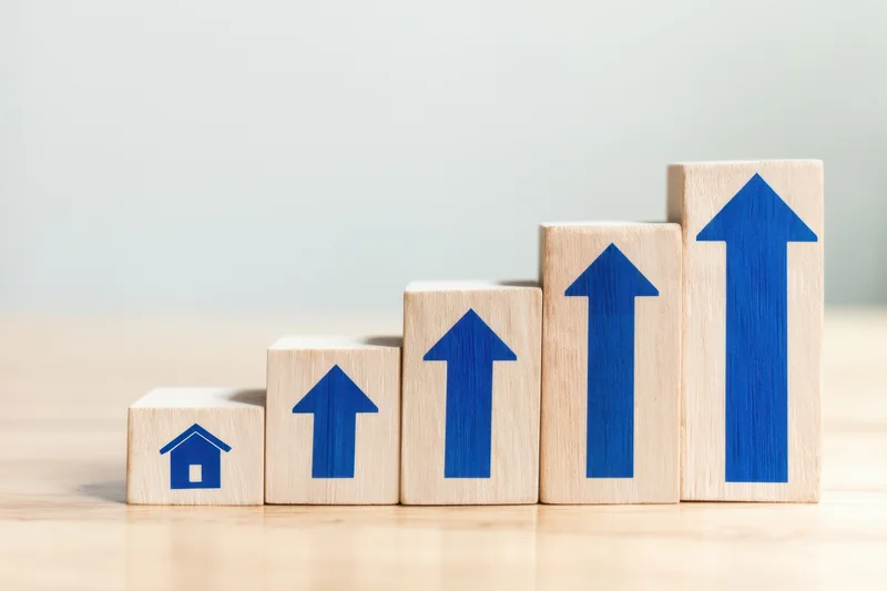 Wooden blocks with blue arrows and house symbol arranged in ascending order on a light surface