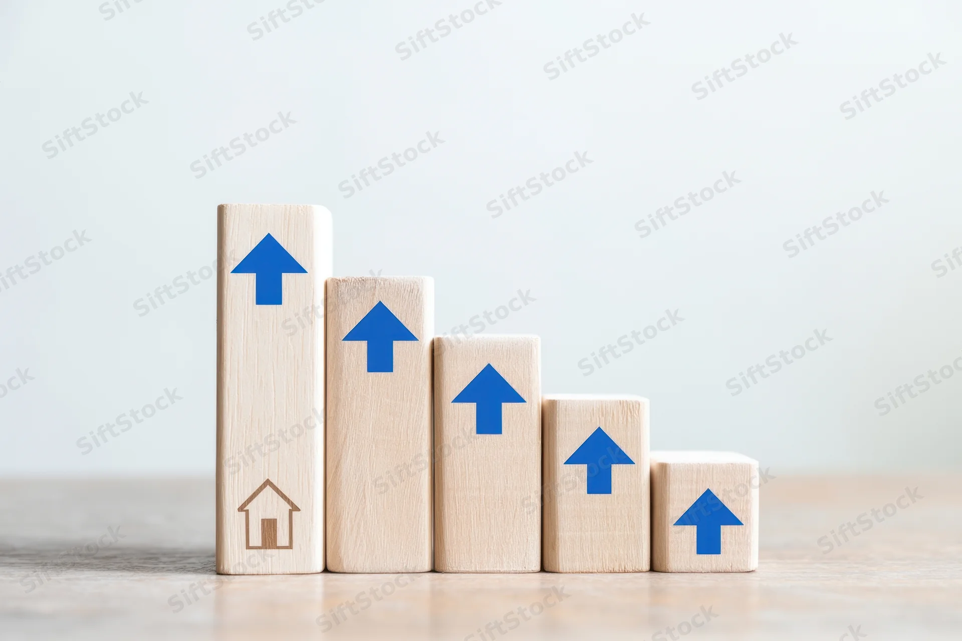 Wooden blocks with blue arrows arranged in descending height on a desk, symbolizing real estate growth and property investment trends