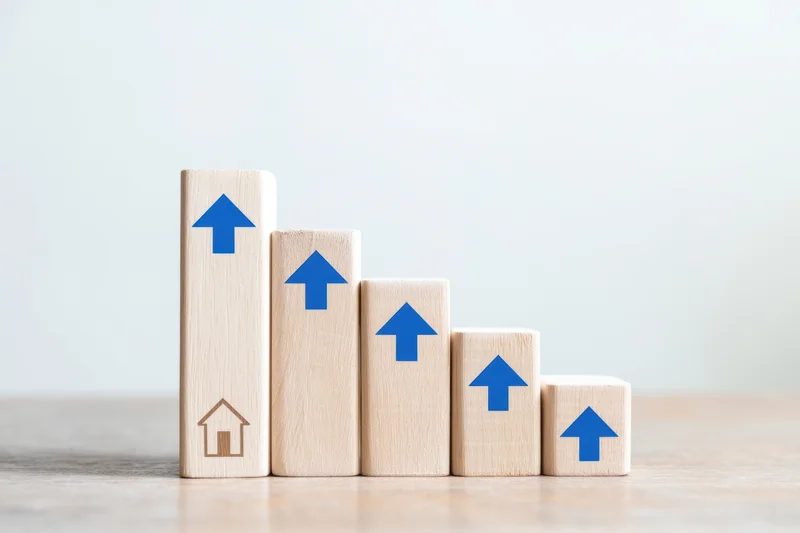 Wooden blocks with blue arrows arranged in descending height on a desk, symbolizing real estate growth and property investment trends