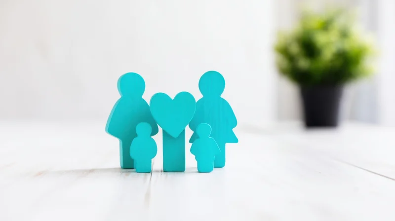 Wooden family figurines with heart symbol on white table near potted plant