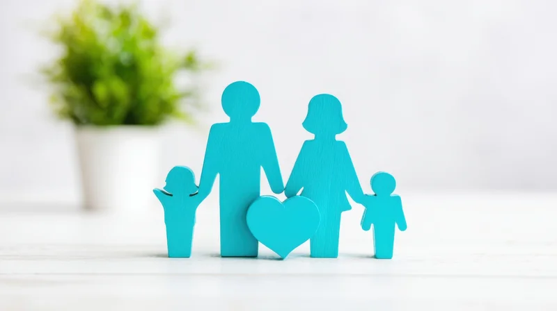 Blue wooden family cutouts with heart symbol on white surface near green plant