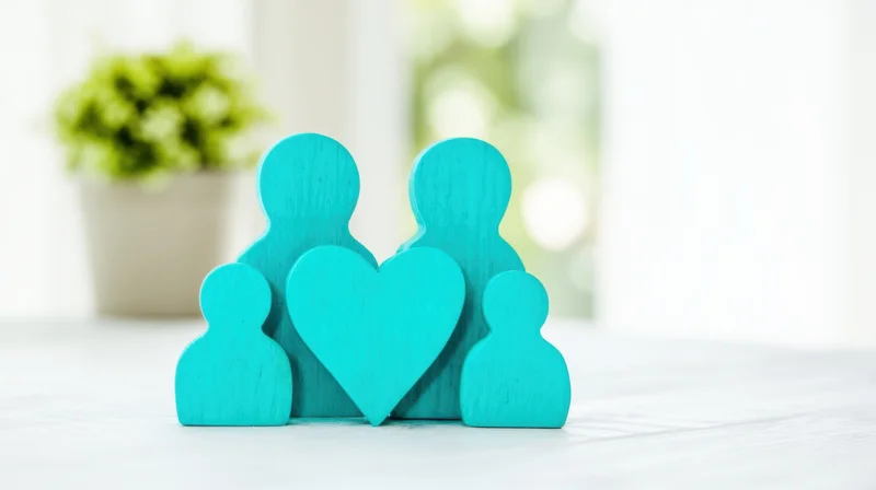 Teal wooden family figurines with heart symbol on white table near plant