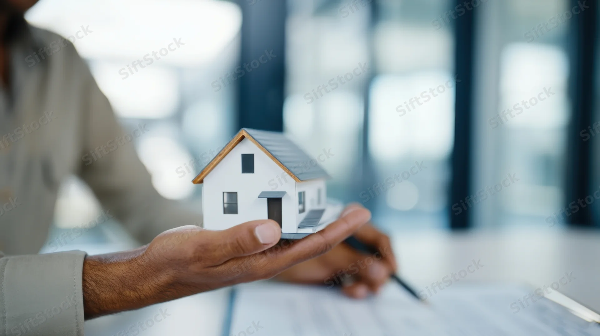 Man holding miniature house model over documents in office