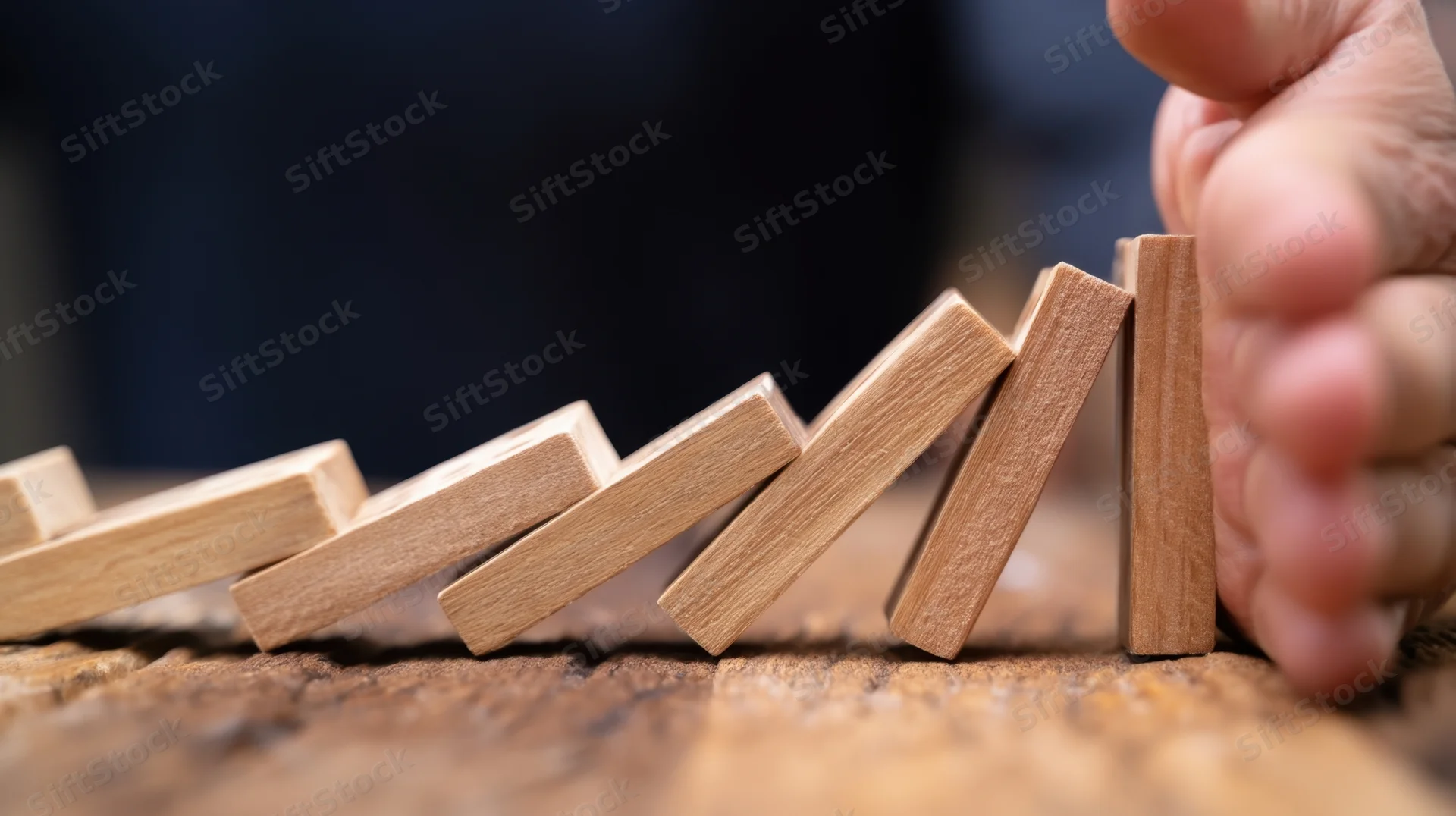Hand stopping a falling line of wooden dominoes on a rustic surface