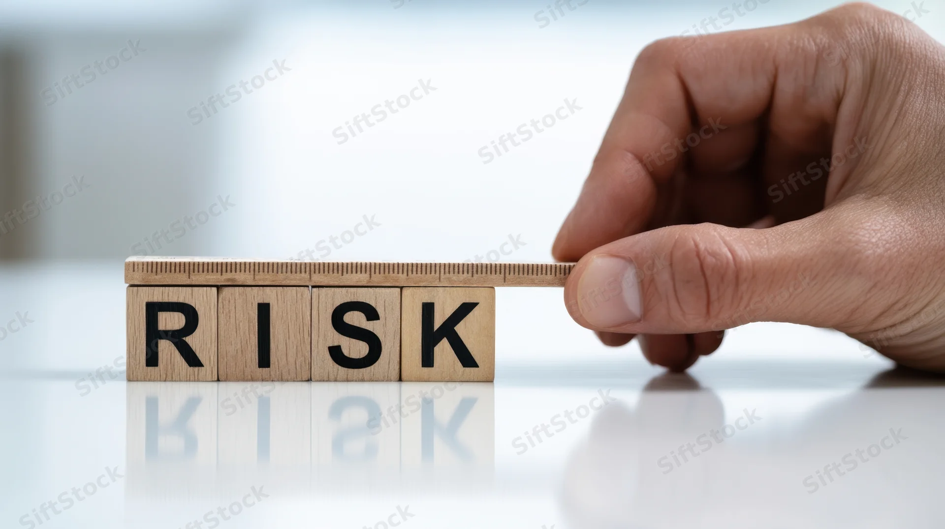 Hand adjusting wooden blocks spelling risk on a reflective desk surface