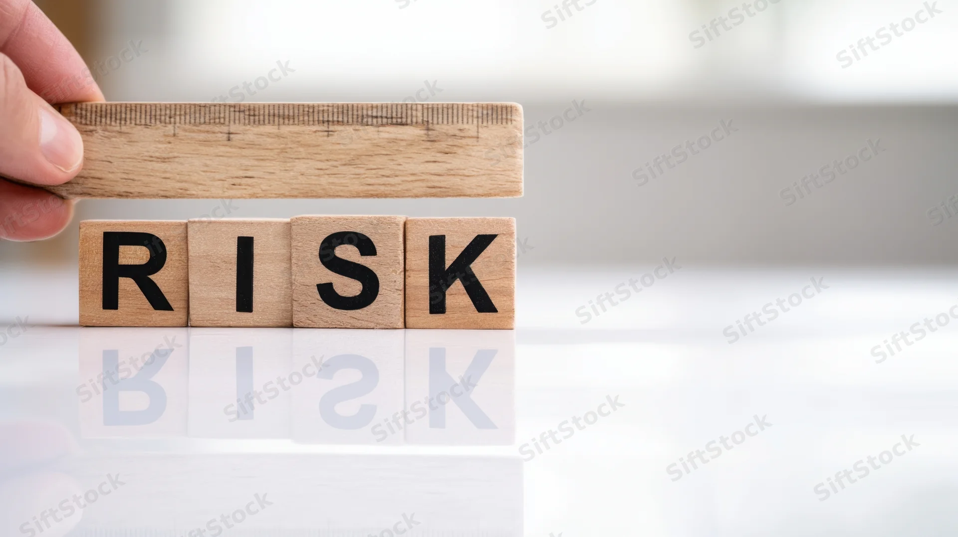 Hand holding ruler over wooden blocks spelling risk on reflective surface