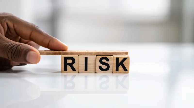 Hand balancing wooden blocks spelling risk on a reflective white surface