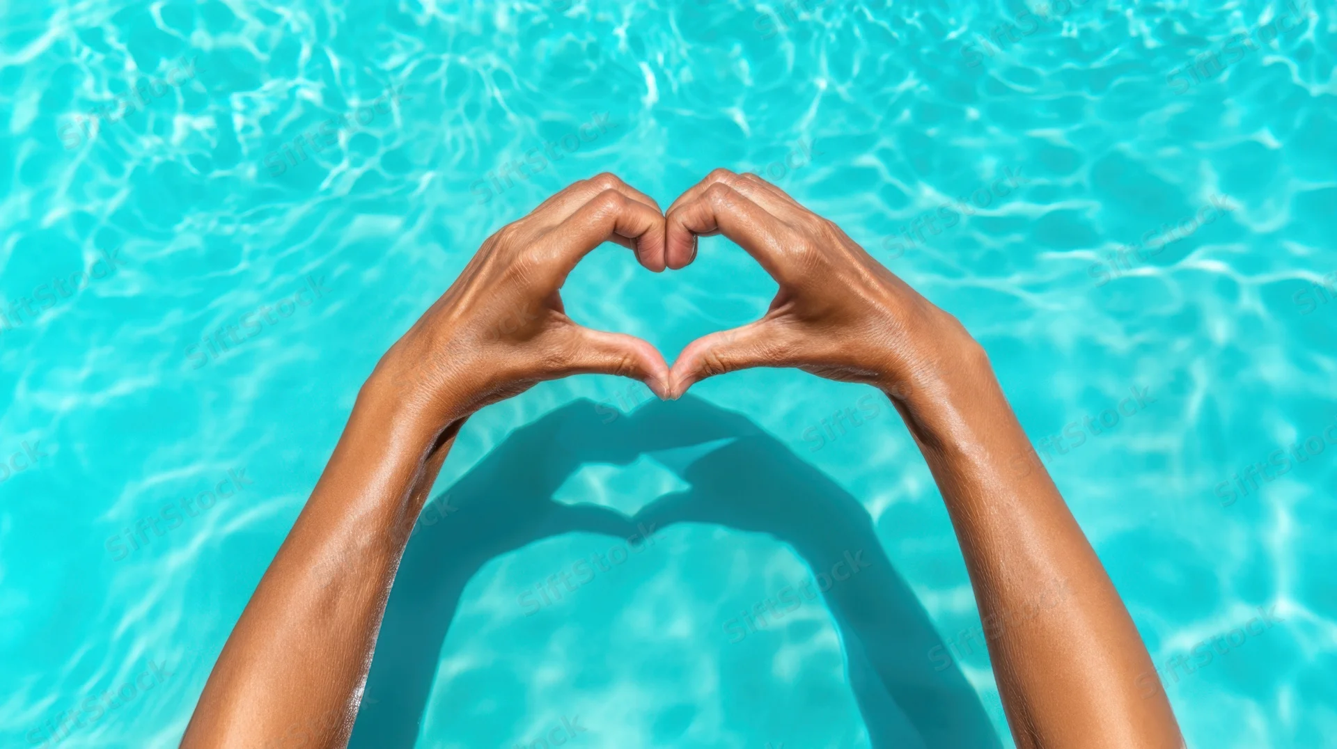 Woman's hands forming heart shape in swimming pool water