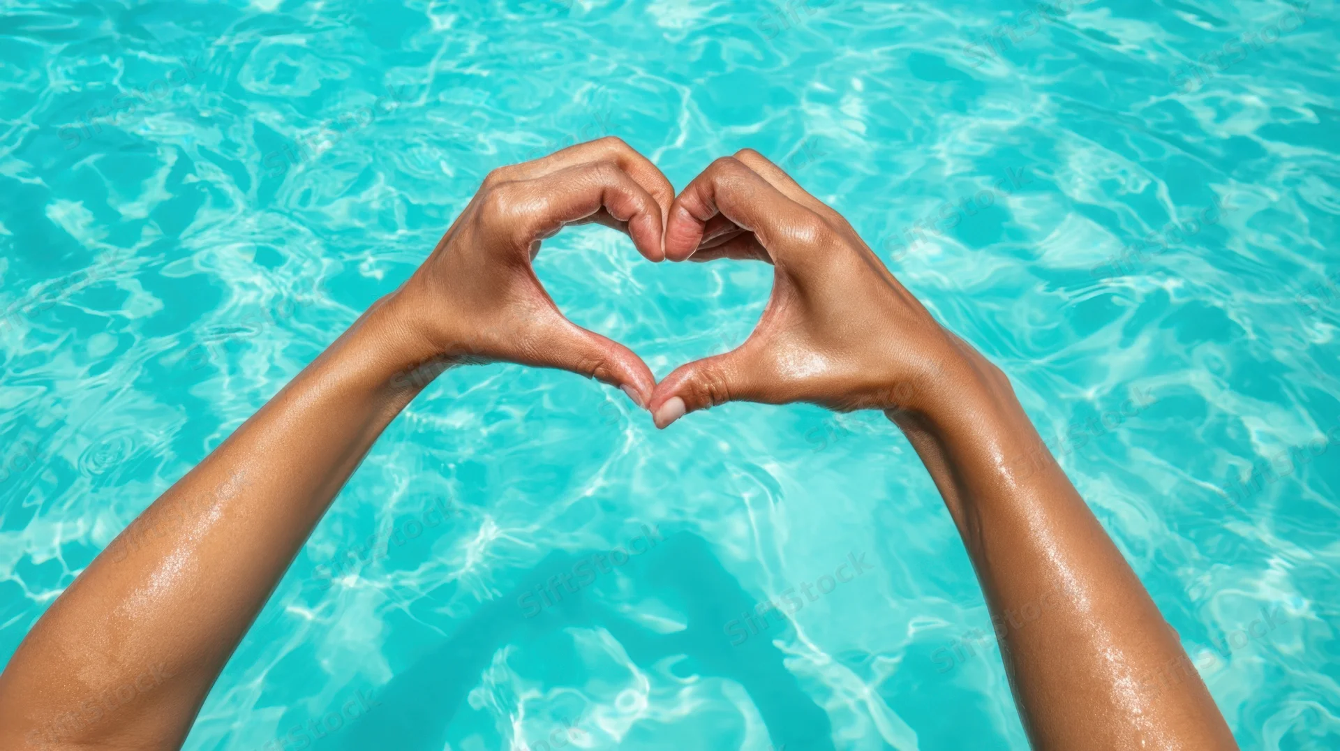 Hands forming heart shape above turquoise pool water