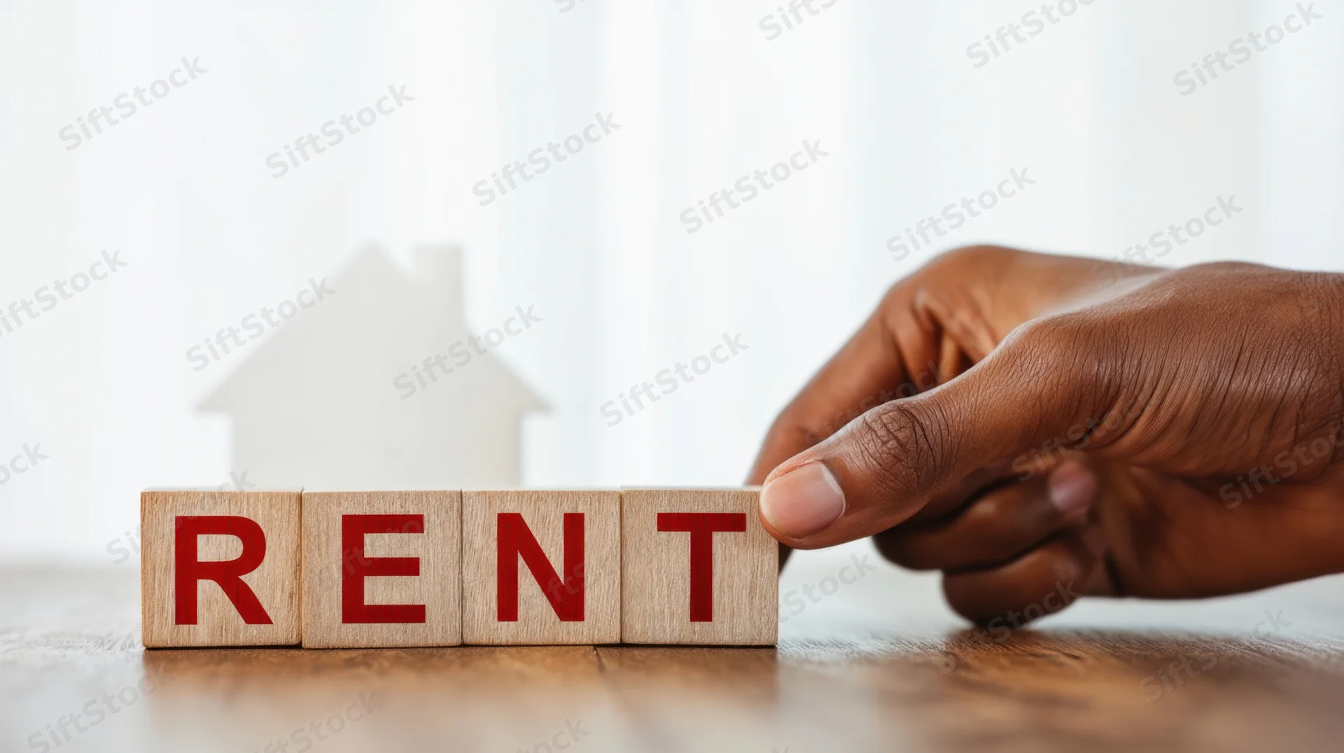 Hand placing wooden blocks spelling rent on a table with a house silhouette in the background