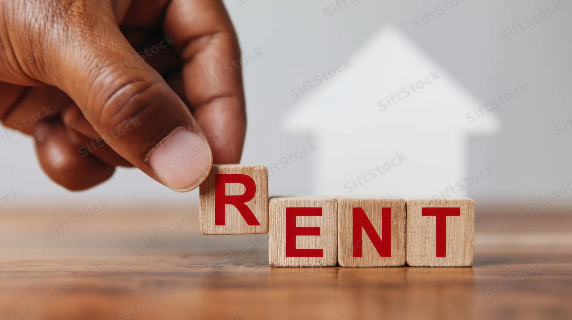 Hand placing wooden block with red letter r to spell rent on wooden table with white house shape in background