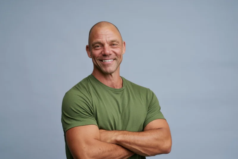 Bald man smiling with arms crossed in green t-shirt against gray background
