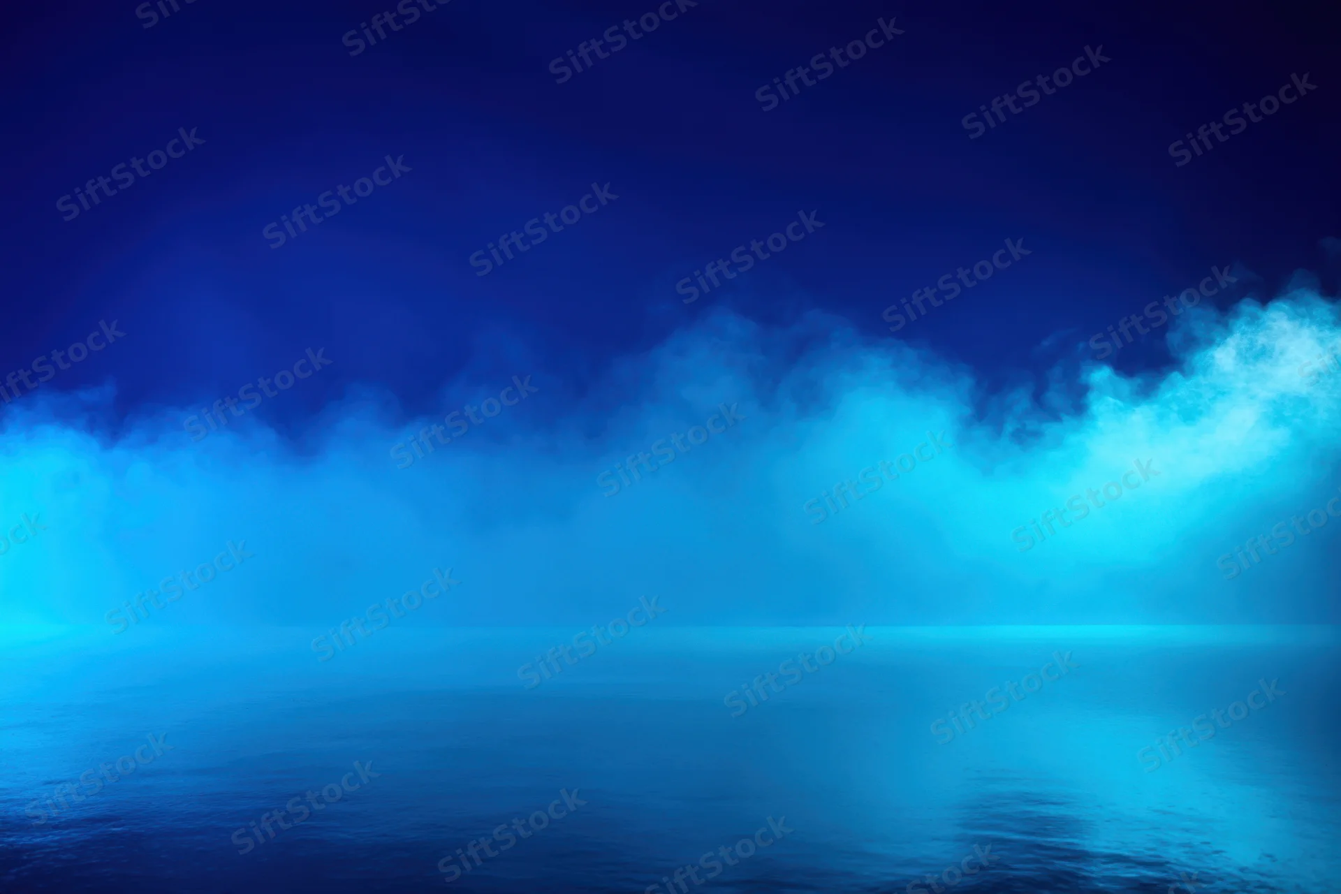 Thick blue fog hovering over a calm reflective surface in a studio setting