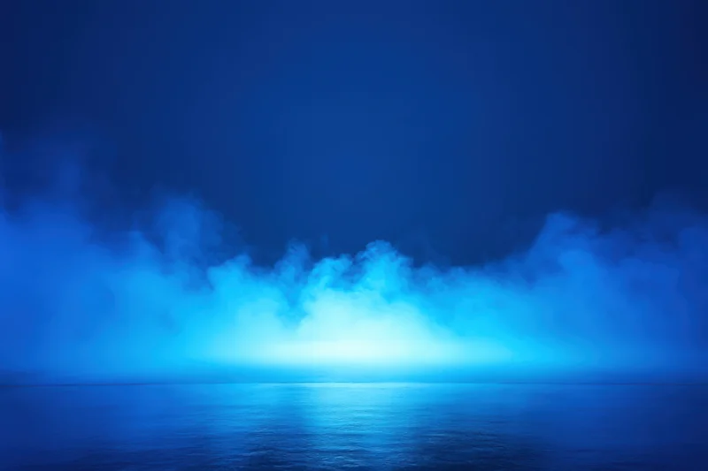 Blue fog over calm water reflecting light at horizon