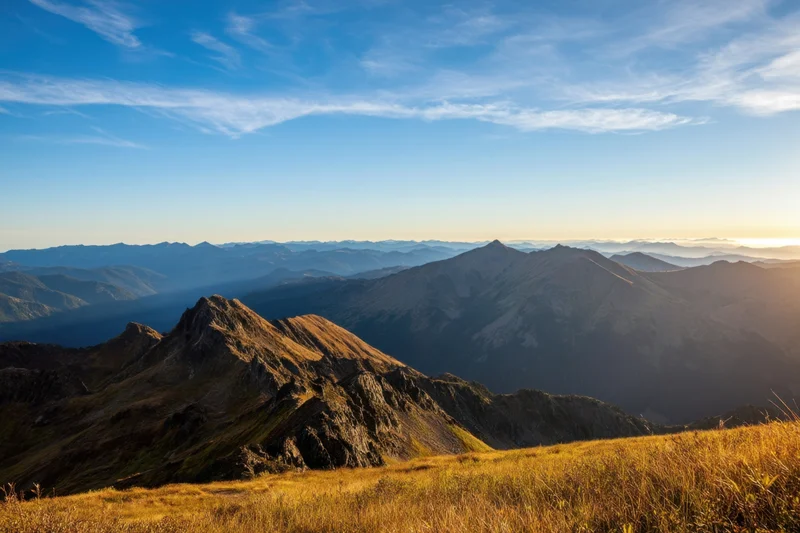 Panoramic mountain vista at sunrise with golden light over alpine peaks and valleys