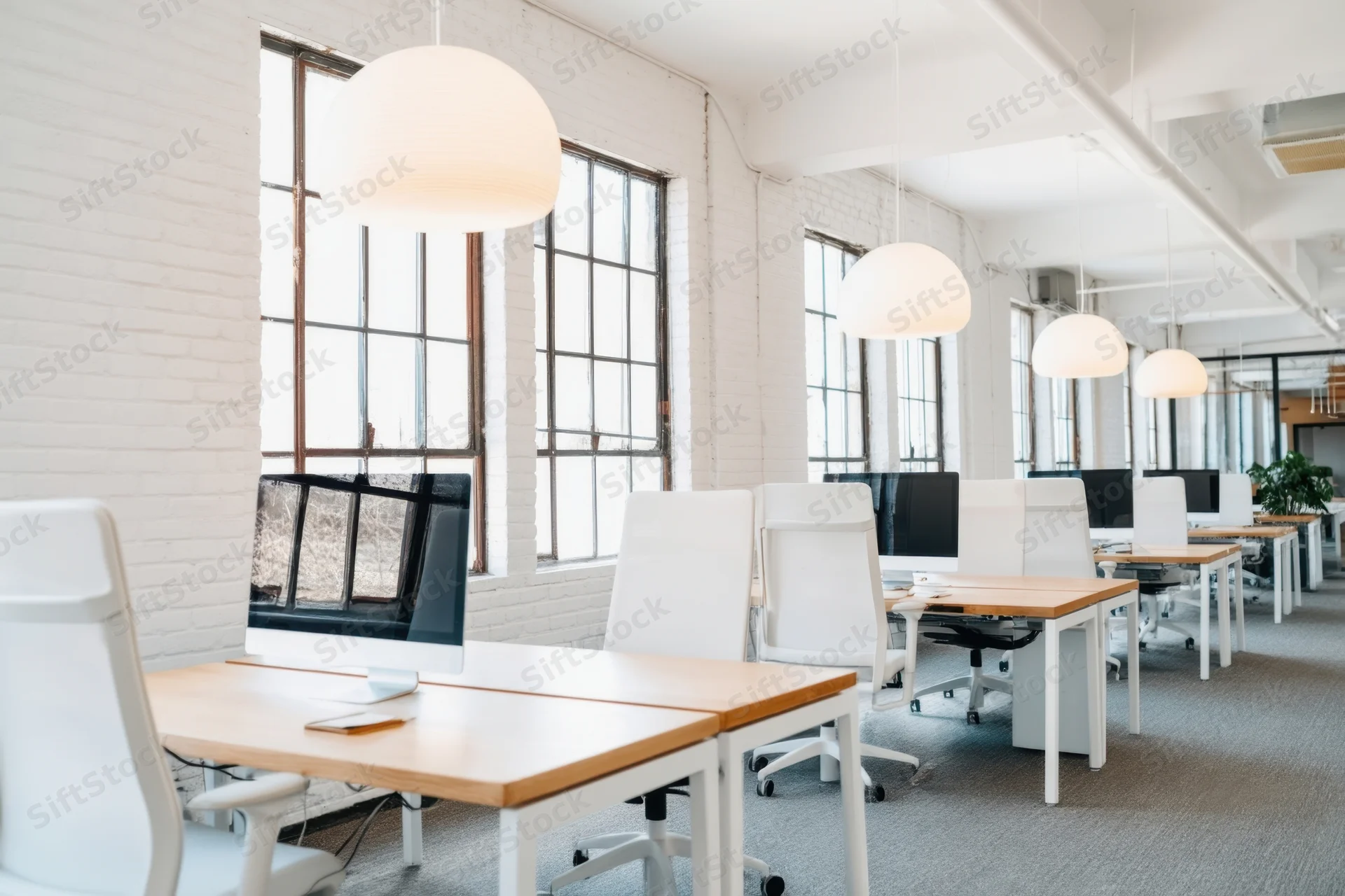 Bright open-plan office with white brick walls and large windows featuring desks, chairs, and pendant lights