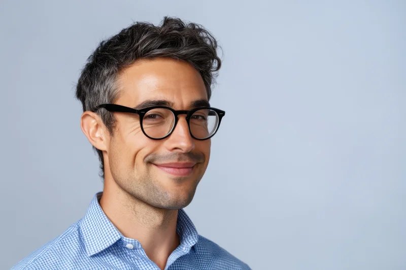 Smiling man with black-rimmed glasses wearing a blue checkered shirt in a studio portrait