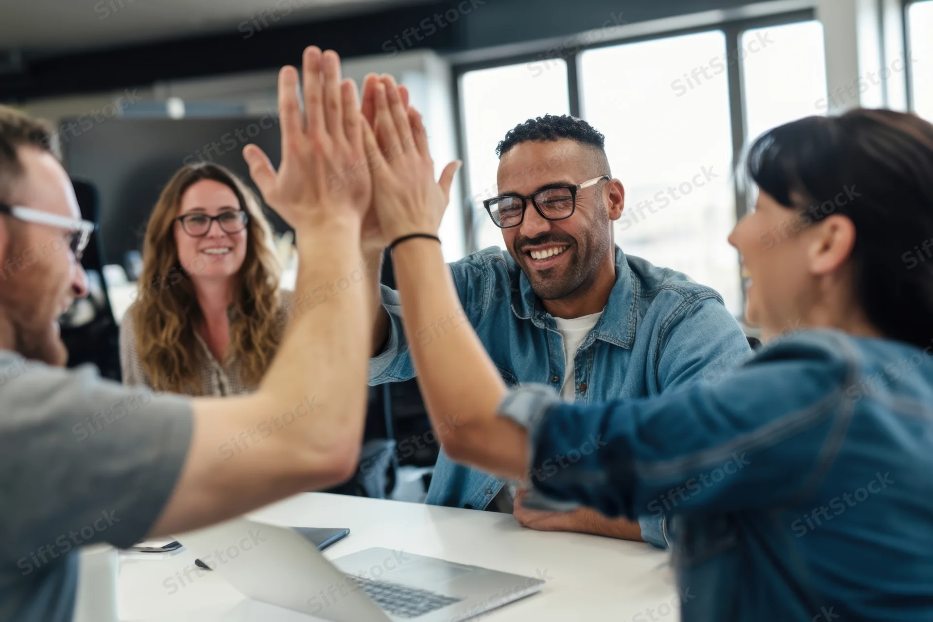 Team members giving high fives at office meeting table