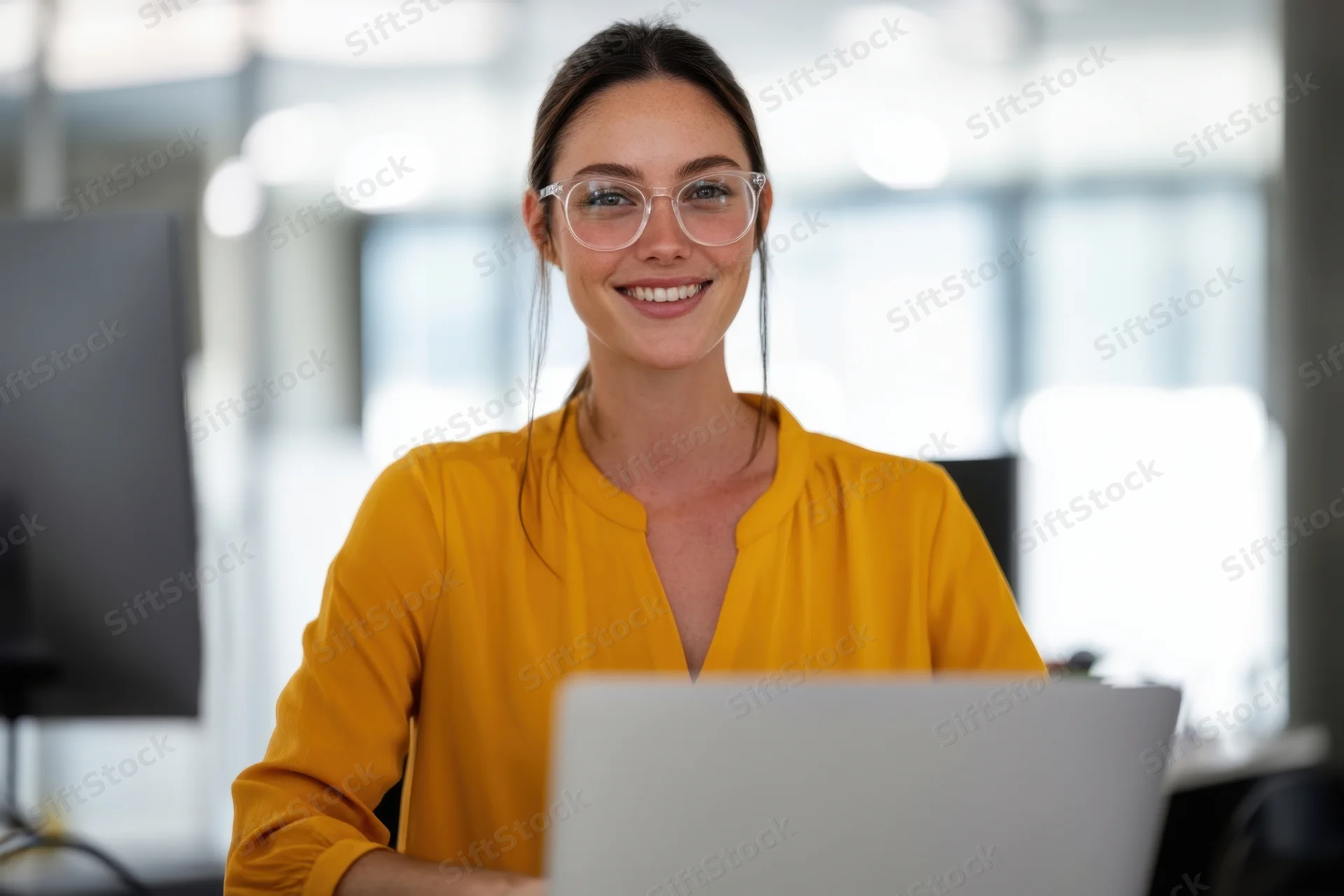 Woman smiling at camera while using laptop in office