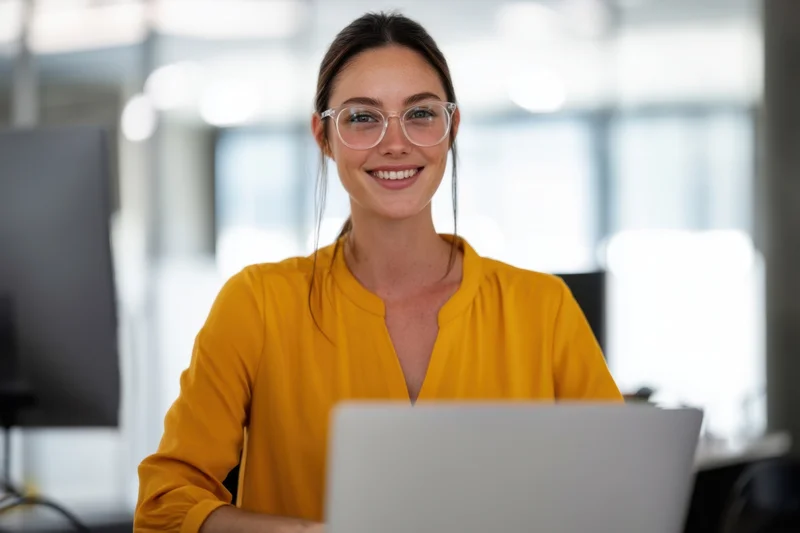 Woman smiling at camera while using laptop in office
