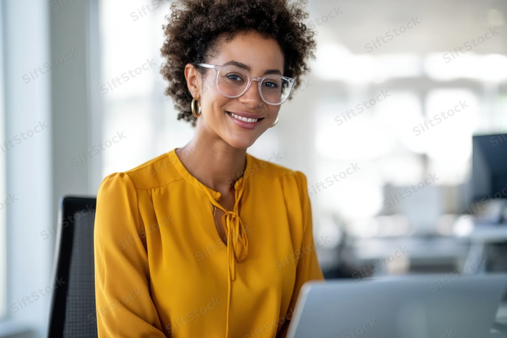 Woman smiling at camera while working on laptop in office