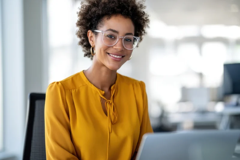 Woman smiling at camera while working on laptop in office
