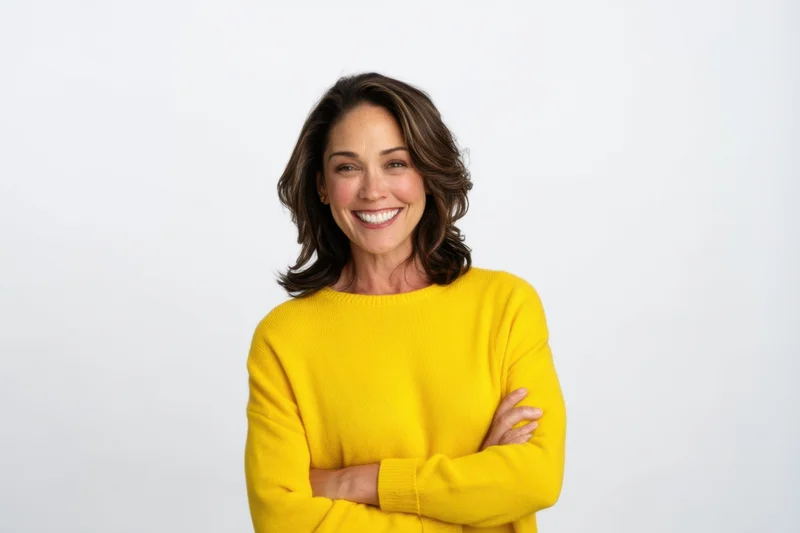 Woman smiling with arms crossed in yellow sweater against white background