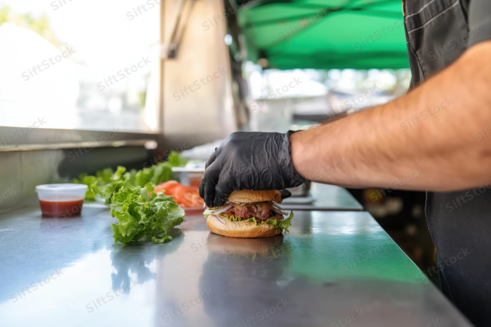Chef assembling burger on stainless steel counter at outdoor food truck