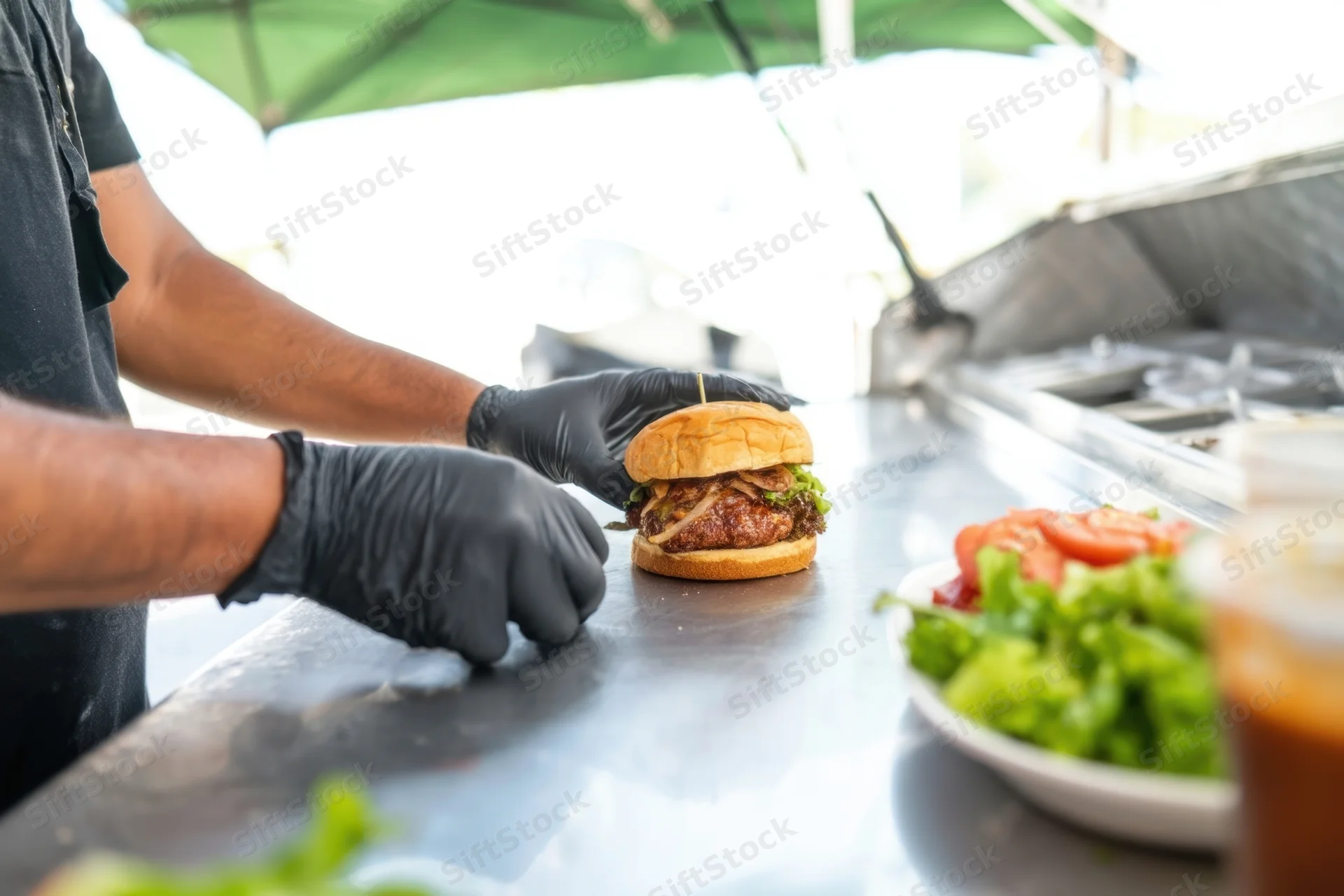 Chef assembling burger on stainless steel counter outdoors
