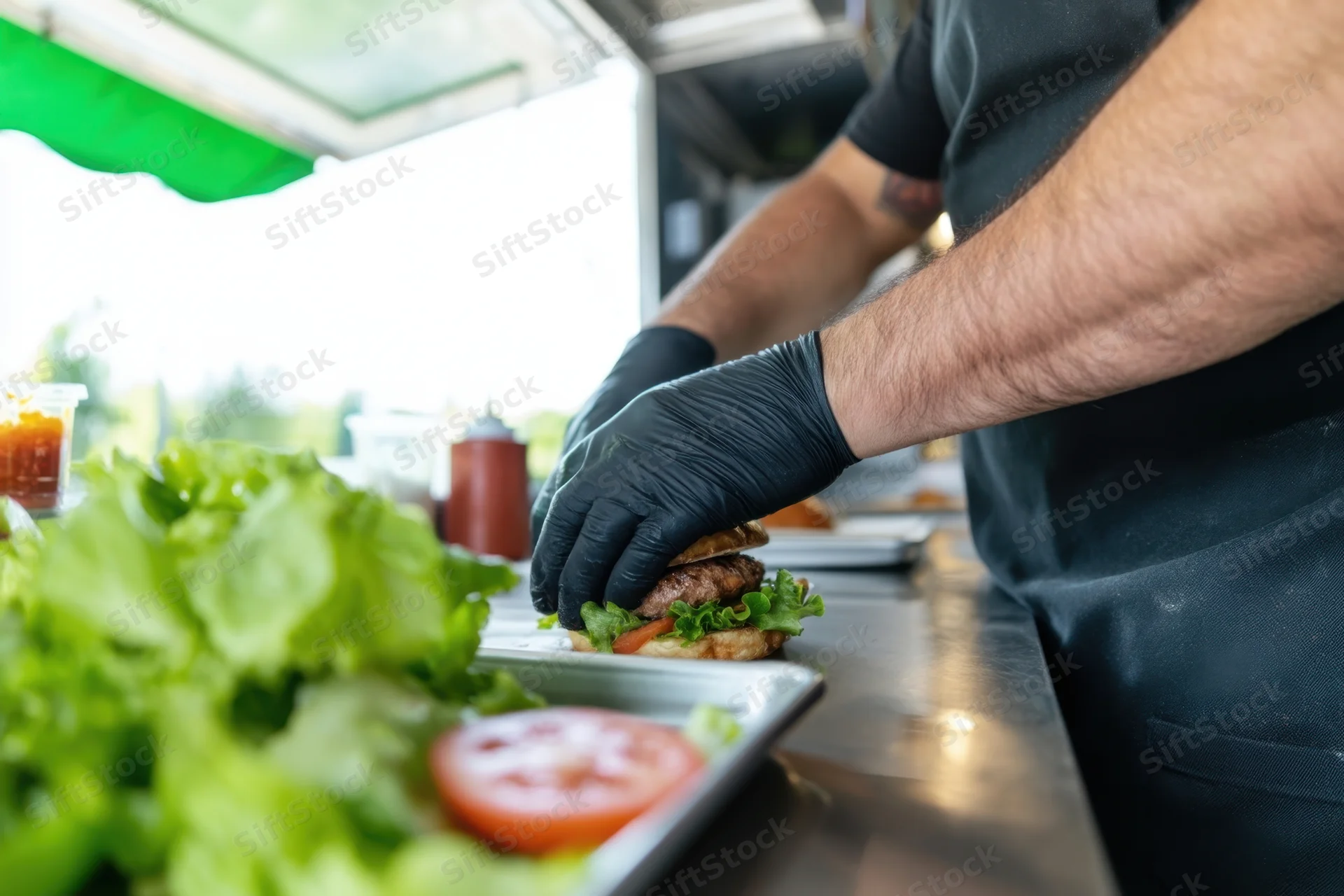 Chef assembling burger with lettuce and tomato on stainless steel counter in food truck kitchen